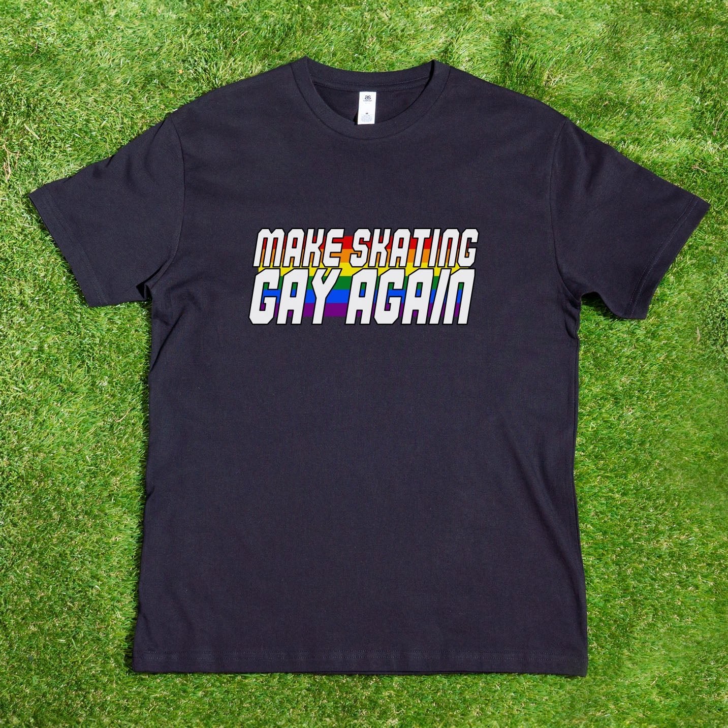 A local hand-printed black T-shirt from My Store sits on grass, showcasing the bold and colorful message "Make Skating Gay Again," embodying the vibrant essence of rainbow pride apparel. Perfect for GAY SKATE events, this unisex shirt is available with shipping within Australia.