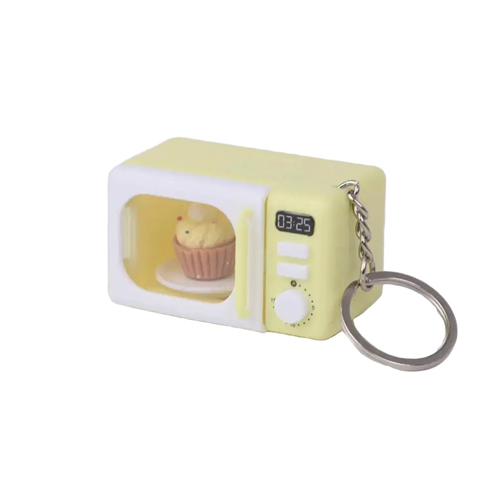 A miniature yellow and white microwave keychain with a small cupcake figurine inside and a metal key ring attached, shown on a clean light gray background.