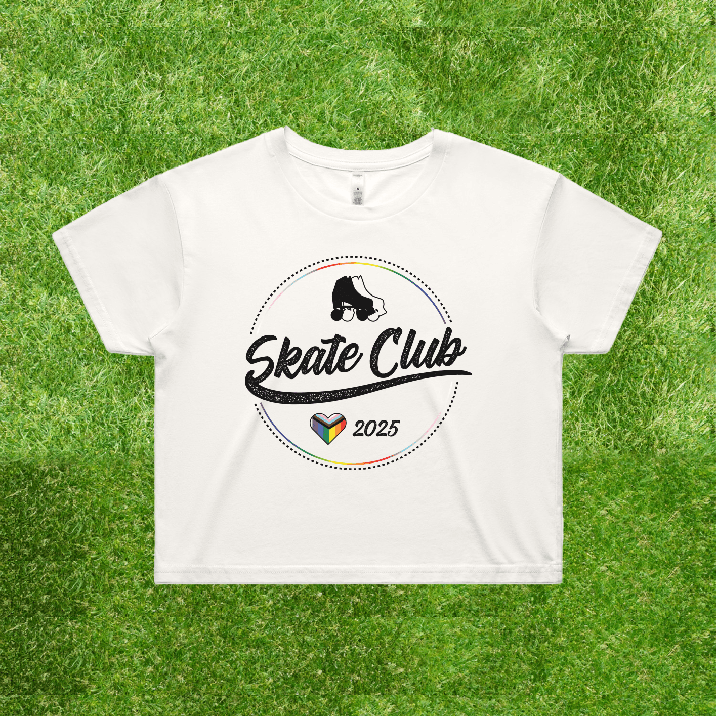 Introducing the NEW!! SKATE CLUB 2025 progress pride crop tee by Gay Skate. This white tee features the Skate Club 2025 logo with stylized text and an illustration of a skateboarder. Below, it incorporates a vibrant heart design that subtly captures the essence of Gay Skate's inclusive vibe, all presented against a natural grassy backdrop for a touch of style and embrace of inclusivity.