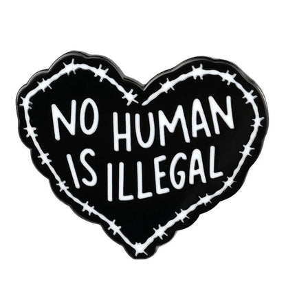 Heart-shaped enamel pin with 'No Human Is Illegal' text surrounded by barbed wire on a white background
