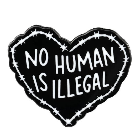 Heart-shaped enamel pin with 'No Human Is Illegal' text surrounded by barbed wire on a white background