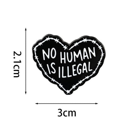 Heart-shaped badge with 'No Human Is Illegal' text and barbed wire design