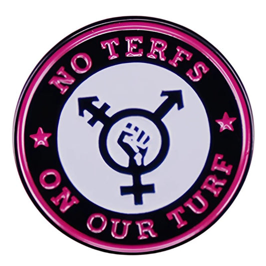 The NO TERFS ON OUR TURF pin by Gay Skate is a circular badge featuring a transgender symbol with a raised fist, set on a black background with a pink border. Surrounding text reads "No TERFs on our turf," accented by stars, taking a stand against transphobia.