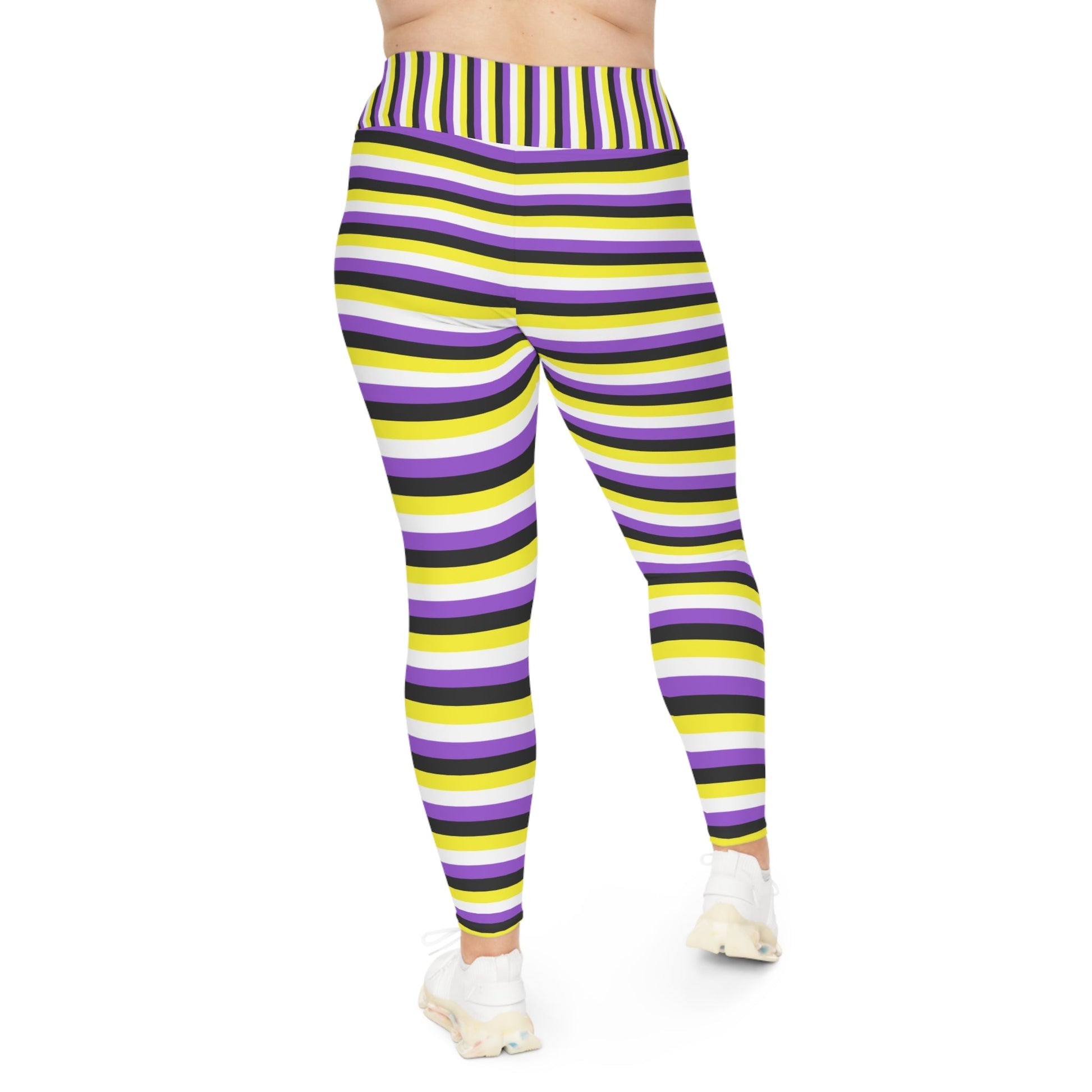 A person wearing Printify's Non-Binary Pride Flag Plus Size Leggings, sizes 2XL - 6XL, which feature high-waisted, colorful horizontal stripes in black, purple, yellow, and white. Made from 4-way stretch fabric for comfort and flexibility, they stand with their feet slightly apart. Only their legs and part of their torso are visible. They are also wearing white sneakers.