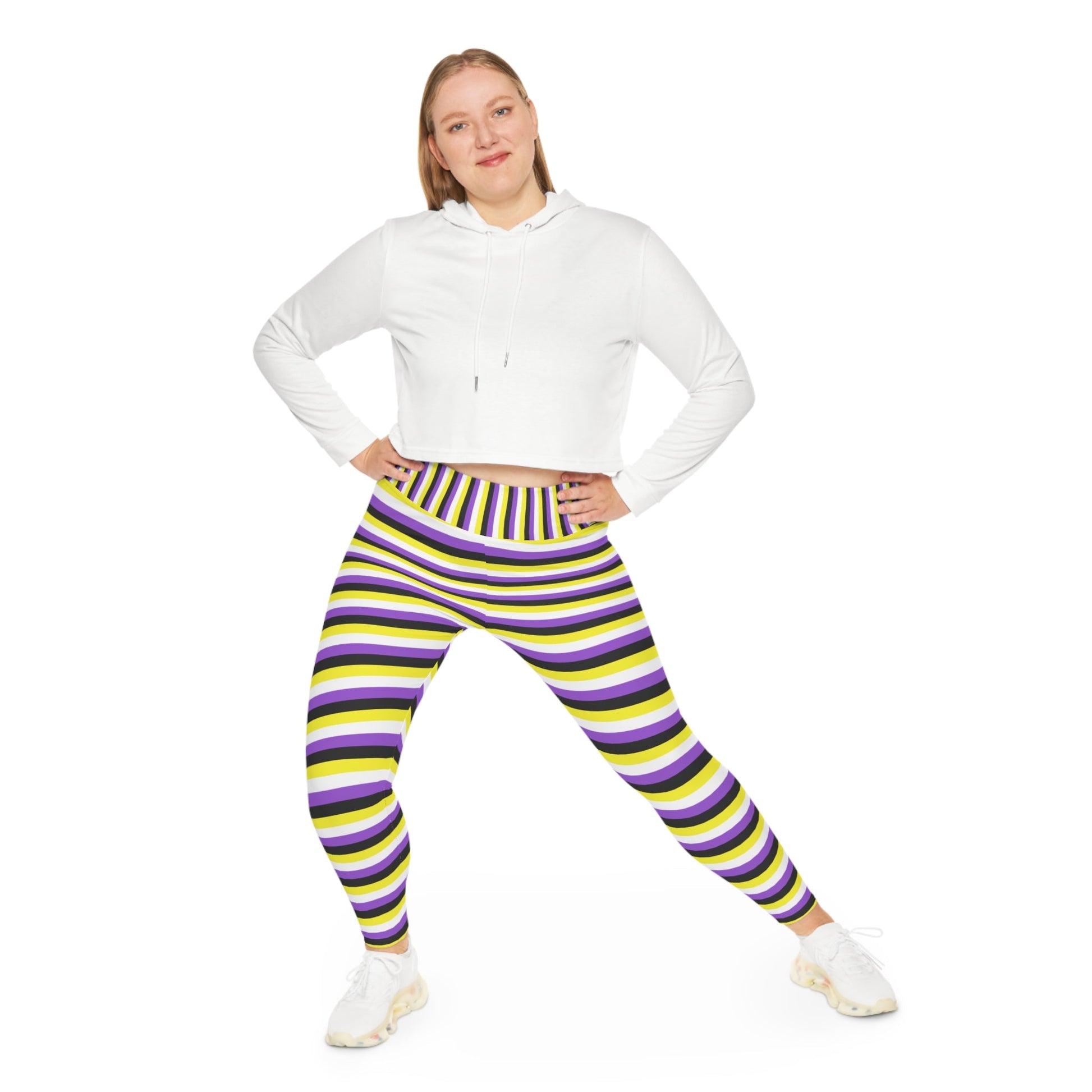 A person wearing Printify's Non-Binary Pride Flag Plus Size Leggings, sizes 2XL - 6XL, which feature high-waisted, colorful horizontal stripes in black, purple, yellow, and white. Made from 4-way stretch fabric for comfort and flexibility, they stand with their feet slightly apart. Only their legs and part of their torso are visible. They are also wearing white sneakers.