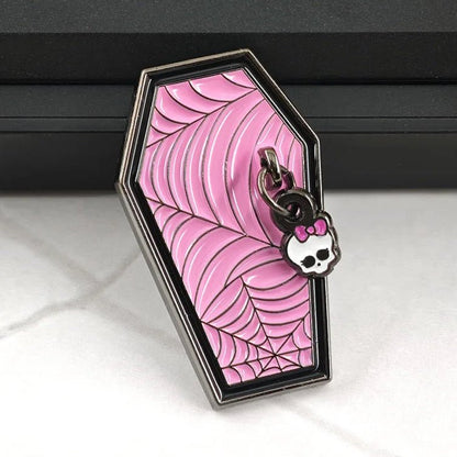 A monster high coffin-shaped pink enamel pin featuring a cobweb pattern with a small Hello Kitty styleskull charm