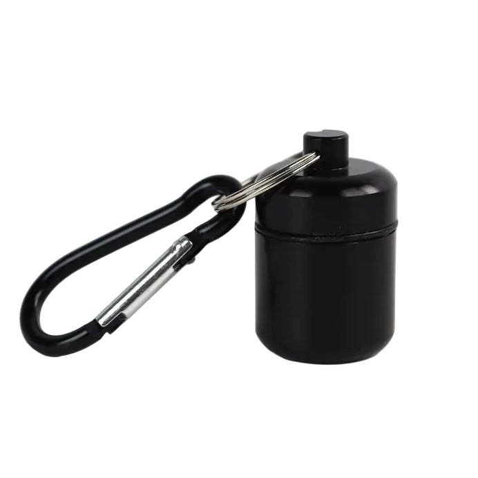 A small black waterproof cylindrical pill container with a screw-top lid, attached to a black carabiner via a small metal keys ring 