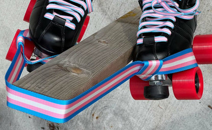 Three skate leashes are shown, each featuring unique striped color patterns: one with the rainbow flag, one with the Trans flag, and one with the Non-Binary flag. Each band has a looped design that can double as a yoga mat strap. These  skate nooses are branded under Gay Skate and named Pride Skate Leash – Gear strap.