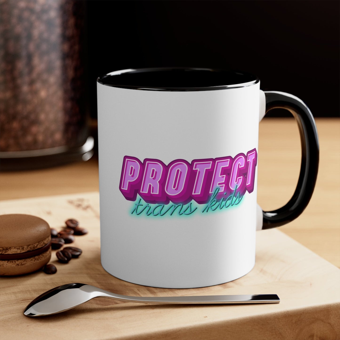 The Protect Trans Kids colourful accent mug by Printify is a white ceramic mug with a black handle and inner rim. It features a vibrant design that says "PROTECT trans kids" in bold, gradient lettering. The word "PROTECT" is in pink and purple, while "trans kids" is in teal, showcasing transgender pride.