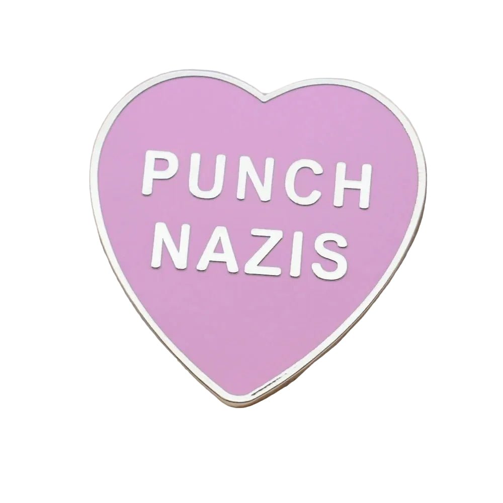 Heart-shaped enamel pin with 'PUNCH NAZIS' text on a wooden surface