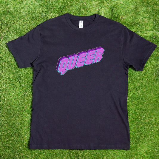 The QUEER neon logo t-shirt, hand printed locally by Gay Skate, boasts bold purple 3D letters spelling "QUEER" on a black fabric, celebrating diversity. It's displayed on green grass and available for custom orders.