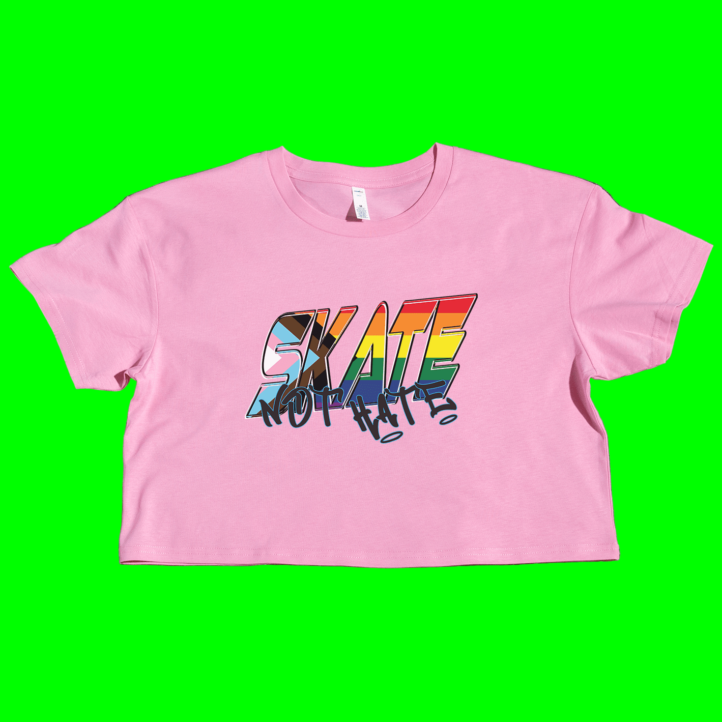 A white cropped t-shirt with the text 'SKATE NOT HATE' printed in rainbow colors on the front, placed on a grassy surface.