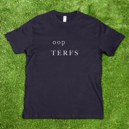 A black AS Colour tee reading "oop TERFS" in white rests on green grass; it’s a [REDACTED] TERFS local, hand-printed t-shirt from a trans and queer-owned brand.