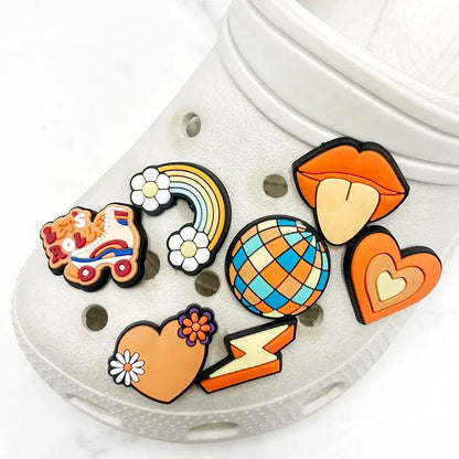 Gay Skate's Retro Roller Skate Shoe Charms feature seven vibrant, retro-themed jibbitz: quad skates with "Let's Roll," a daisy, rainbow, lips with tongue, disco ball, and two heart designs (one as a lightning bolt) on chic white shoes.