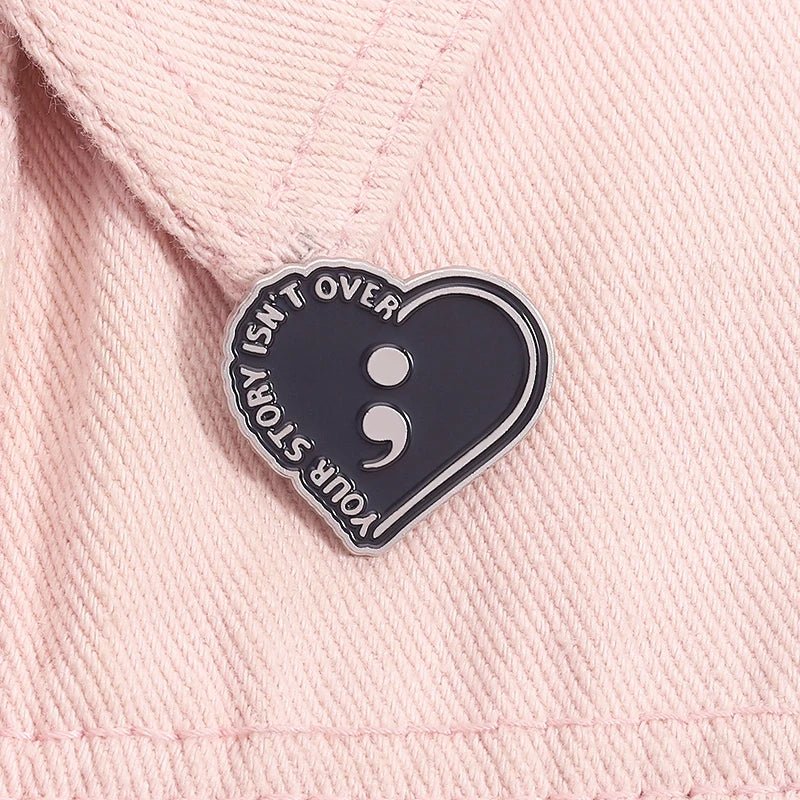 Your Story Isn't Over - Heart-shaped black enamel pin with semicolon symbol. Mental health awareness