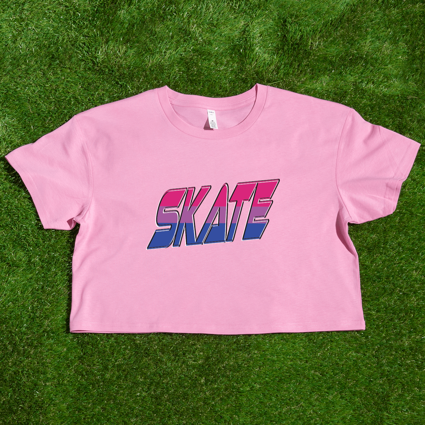 The "SKATE bisexual pride flag - locally printed crop tee" by Gay Skate is a black cropped T-shirt featuring the word "SKATE" printed across the front in a bold, gradient design that transitions from red at the top to pink, purple, and blue at the bottom. Perfect for Queer Skate events, it showcases text with a slightly 3D effect and a retro, angular font style.