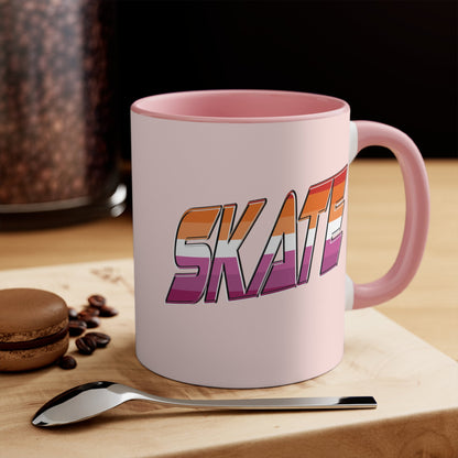 The SKATE lesbian pride flag accent mug by Printify features a bold "SKATE" design in gradient colors of orange, pink, and purple. This eye-catching ceramic mug boasts a light pink handle and interior that beautifully contrast with its pale pink exterior.