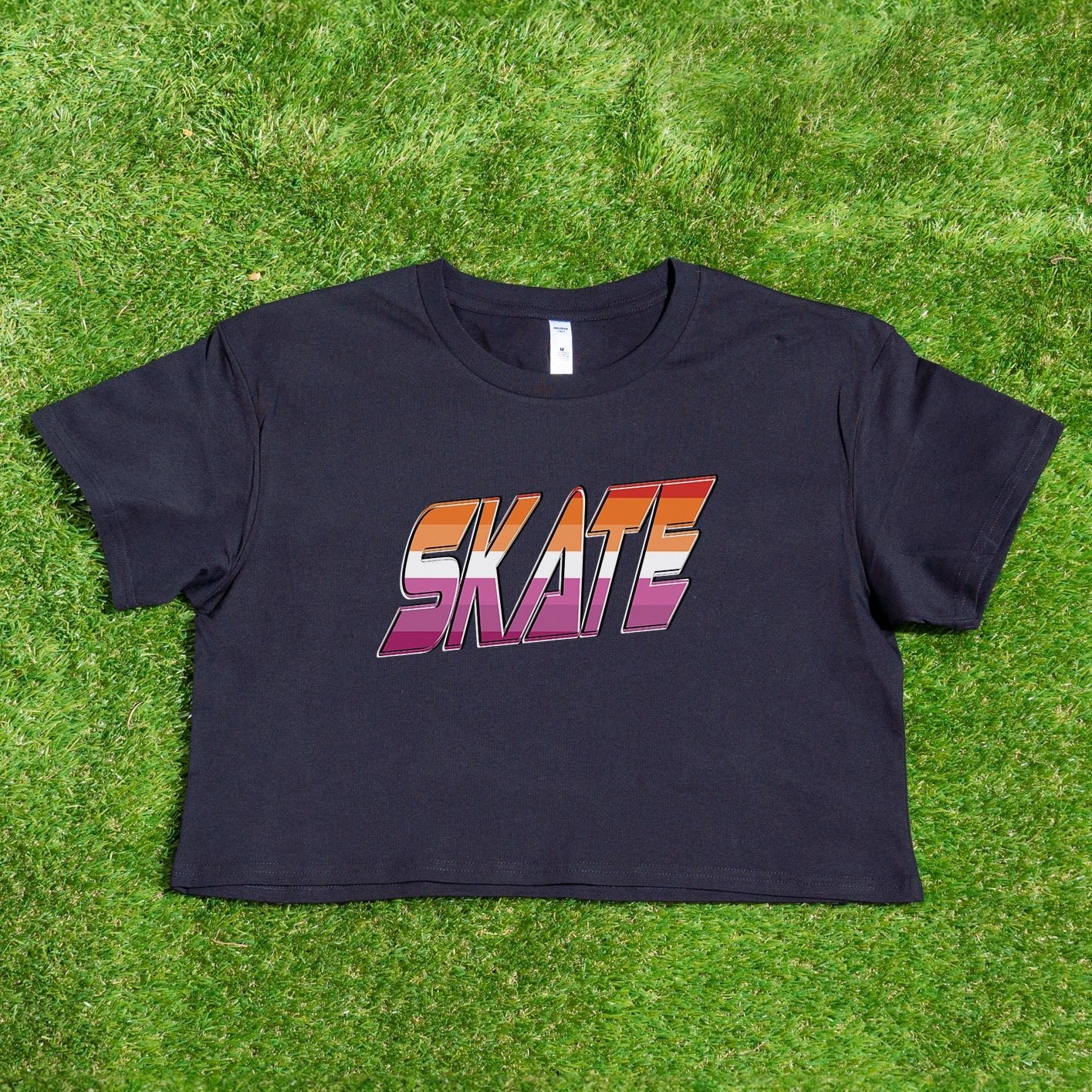 Gay Skate's SKATE lesbian pride flag - locally printed crop tee is a white cropped shirt featuring the word "SKATE" in bold, gradient letters transitioning from orange to pink. The retro, 3D-style lettering adds a distinct flair to this queer skate streetwear piece, which also includes short sleeves and a round neckline.