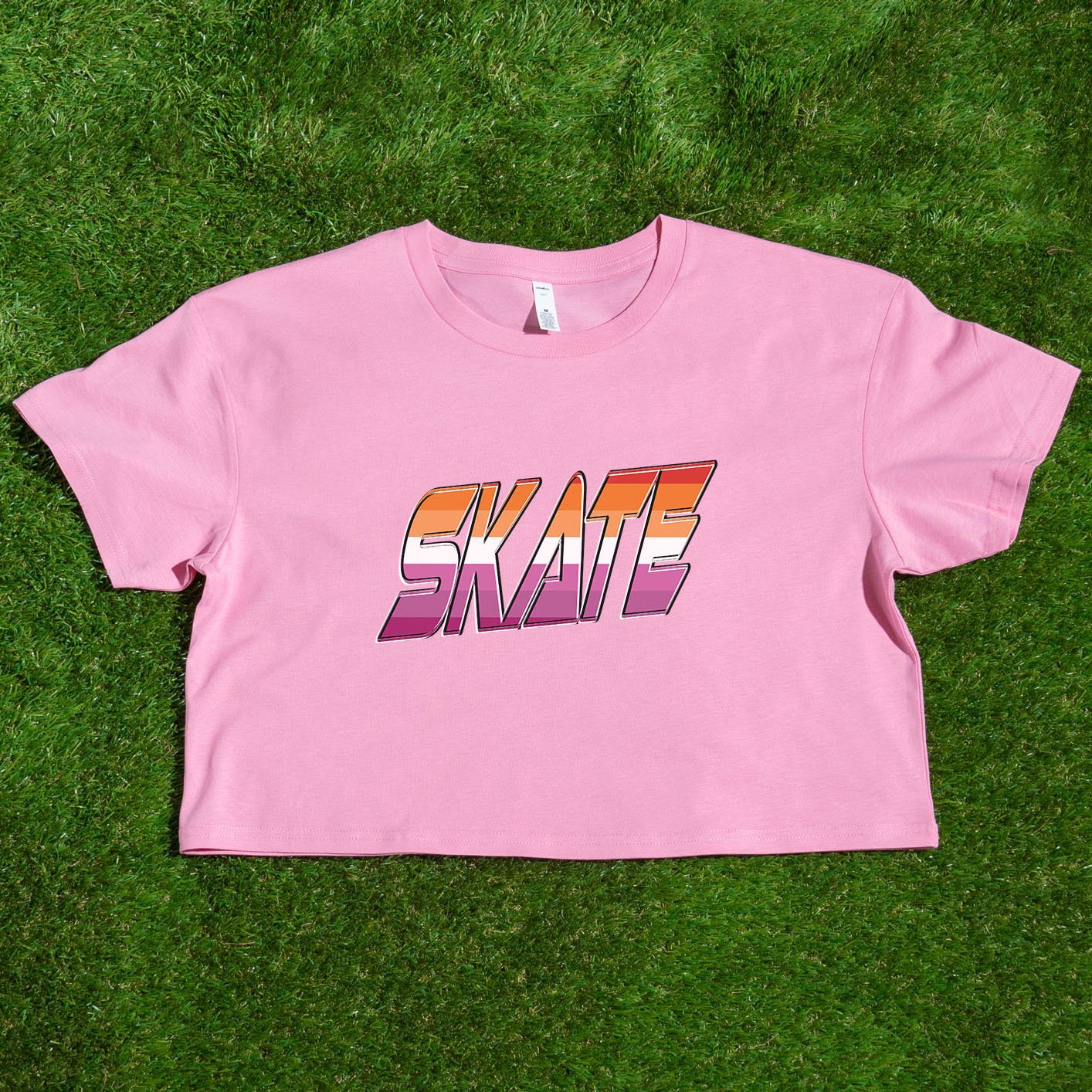 Gay Skate's SKATE lesbian pride flag - locally printed crop tee is a white cropped shirt featuring the word "SKATE" in bold, gradient letters transitioning from orange to pink. The retro, 3D-style lettering adds a distinct flair to this queer skate streetwear piece, which also includes short sleeves and a round neckline.