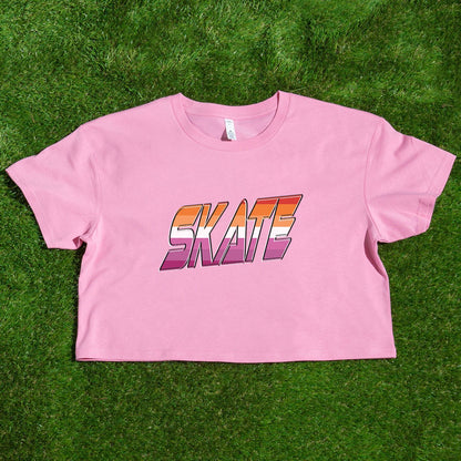 Gay Skate's SKATE lesbian pride flag - locally printed crop tee is a white cropped shirt featuring the word "SKATE" in bold, gradient letters transitioning from orange to pink. The retro, 3D-style lettering adds a distinct flair to this queer skate streetwear piece, which also includes short sleeves and a round neckline.