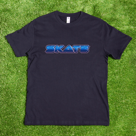 A black t-shirt from Gay Skate, featuring a vibrant SKATE neon logo in multicolored, retro-style letters and locally hand-printed, is laid flat on a background of green grass.