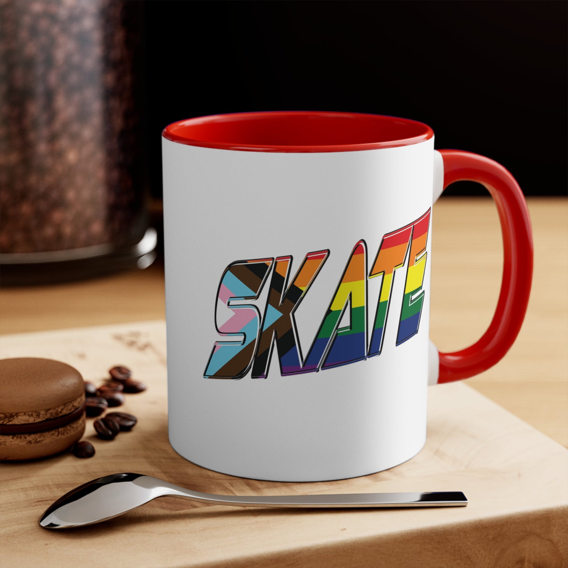 The SKATE progress pride flag accent mug by Printify features a white coffee mug with a red handle and a colorful interior. The front boldly displays the word "SKATE" in rainbow colors, including shades of blue, pink, white, and brown.