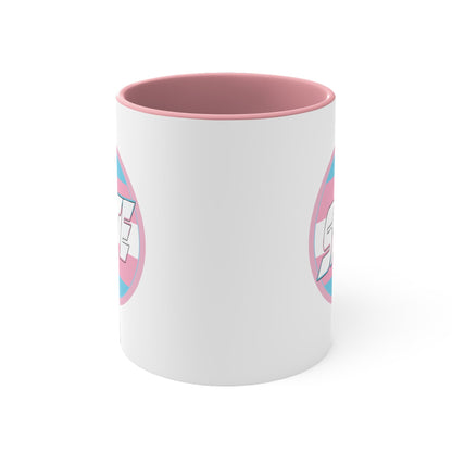 The SKATE trans flag circle design accent mug by Printify features a white exterior, blue handle, and blue interior. It showcases a circular design inspired by the trans flag, incorporating pink, light blue, and white colors. The word "SKATE" is prominently displayed in dynamic white letters at the center of the design.