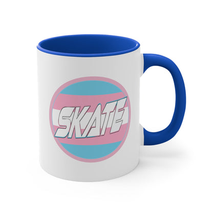 The SKATE trans flag circle design accent mug by Printify features a white exterior, blue handle, and blue interior. It showcases a circular design inspired by the trans flag, incorporating pink, light blue, and white colors. The word "SKATE" is prominently displayed in dynamic white letters at the center of the design.