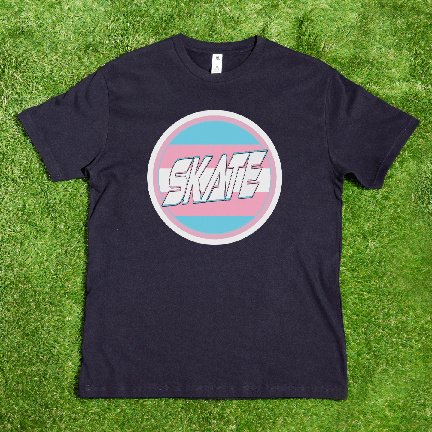 The product is a "Trans Flag Circle Gay Skate - Local hand pressed t-shirt" by Gay Skate. This black, 100% cotton t-shirt features a circular graphic in the center with the word "SKATE" in stylized white text. The graphic has a pink, blue, and white color scheme that resembles the Trans Pride flag, perfect for showing off your Gay Skate pride. The shirt is displayed on a plain white background.