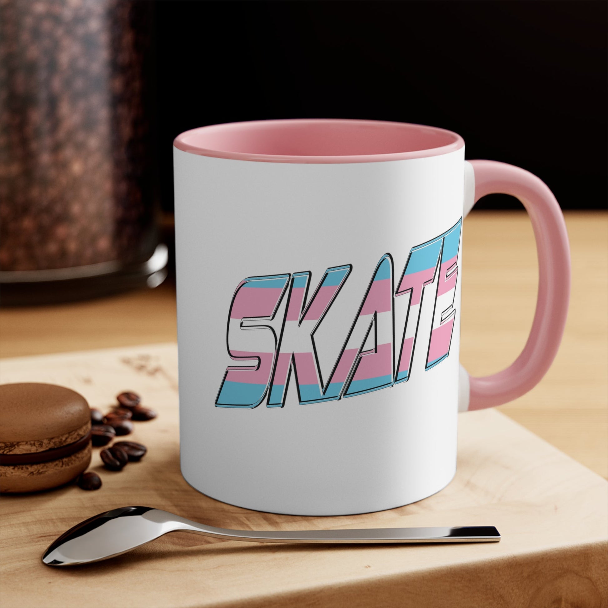 This SKATE trans pride flag accent mug by Printify features a white ceramic base with a blue handle and matching colorful interior. The word "SKATE" is emblazoned in bold letters, styled with vibrant pink and blue tones. Hand wash only to maintain its vivid design.