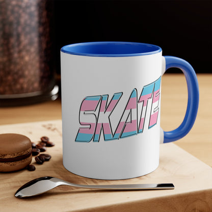 This SKATE trans pride flag accent mug by Printify features a white ceramic base with a blue handle and matching colorful interior. The word "SKATE" is emblazoned in bold letters, styled with vibrant pink and blue tones. Hand wash only to maintain its vivid design.