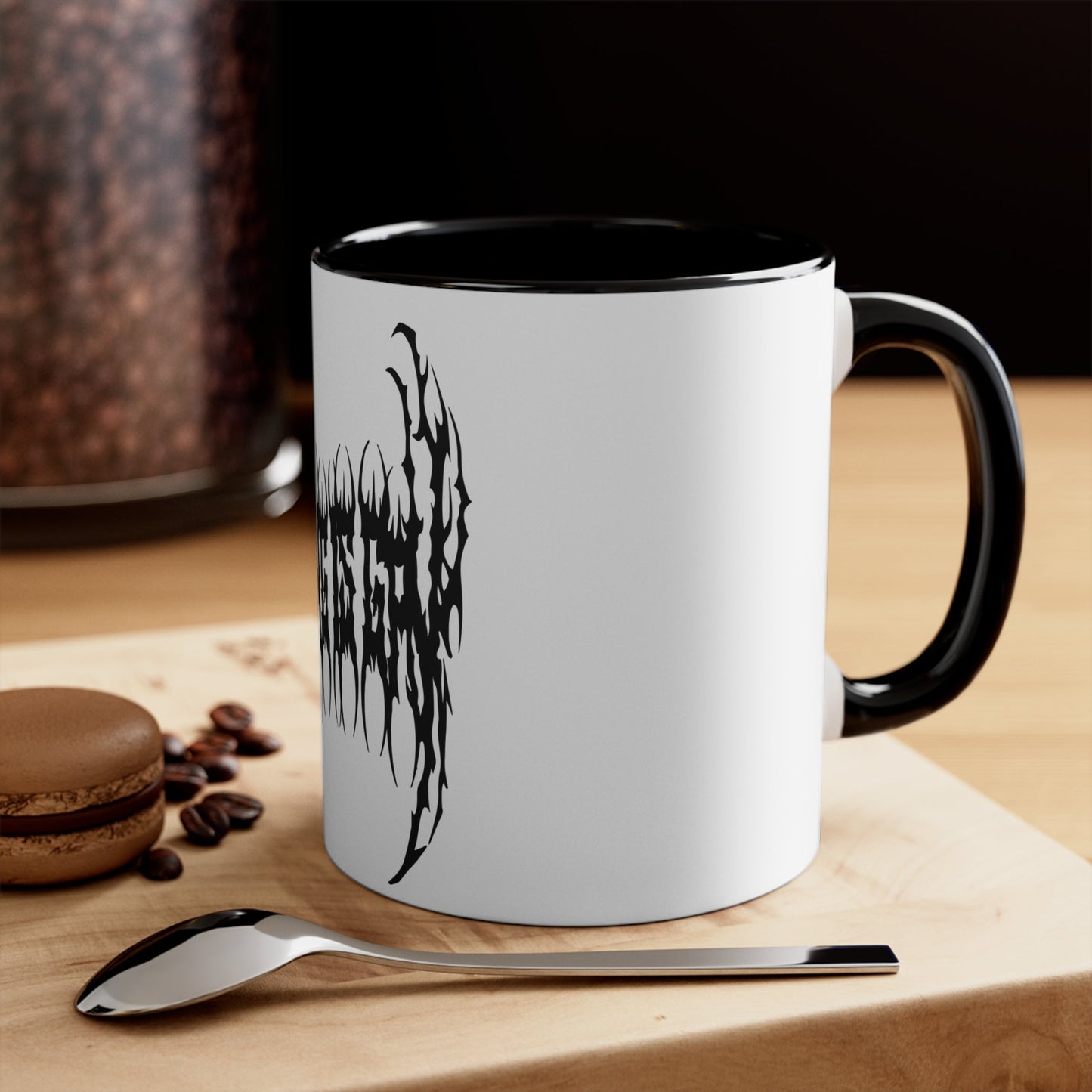 The "SKATING IS GAY but make it death metal accent mug" by Printify is a white mug with a black interior featuring an intricate design that resembles sharp, thorny text. Styled in a death metal font, the symmetrical design has an aggressive, edgy appearance that makes the text difficult to read due to its complex, spiky style.