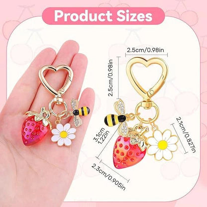 Keychain with strawberry, bee, and flower charms held in a hand, with product size measurements on a pink background.