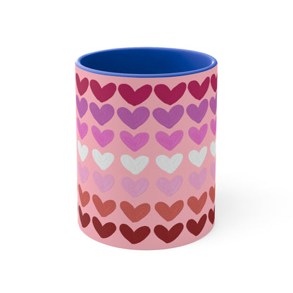 The "Subtle Lesbian Pride Flag - love hearts - colourful accent mug" by Printify is a white ceramic mug with a vibrant interior and red handle, adorned with heart patterns in various shades of pink, purple, and red. The hearts are arranged in horizontal rows, gradually transitioning from lighter shades at the top to darker ones at the bottom.