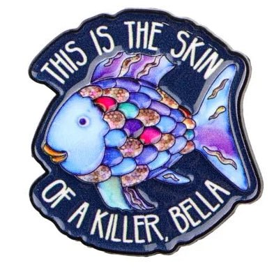 Colorful rainbow fish enamel pin with shimmering scales, featuring the bold white text “THIS IS THE SKIN OF A KILLER, BELLA” on a dark background.