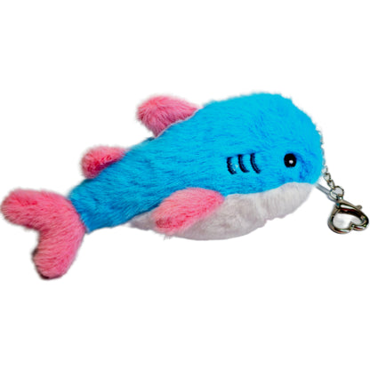 15 cm blue, pink and white trans pride plush shark keychain lying beside its silver-tone heart-shaped carabiner and keyring.