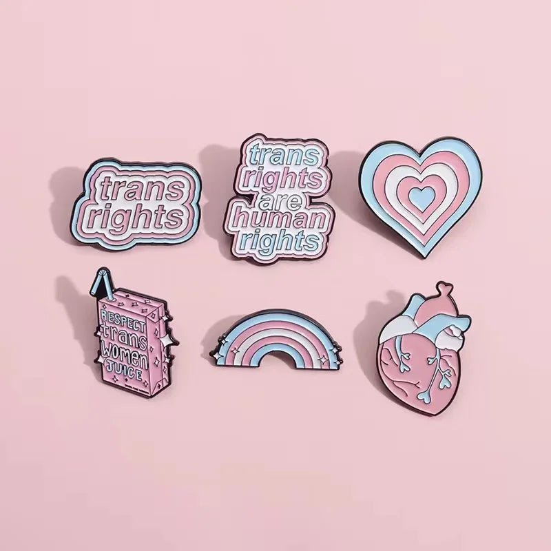 Product Description: The "Trans Rights and Trans Pride" enamel pins collection by Gay Skate includes six beautifully designed badges celebrating transgender pride. Top row designs feature: "Trans Rights Are Human Rights," "Trans Rights," and "Respect Trans Women Juice." Bottom row designs include an anatomical heart with trans flag colors, a heart with layered trans flag colors, and a rainbow with trans flag colors.