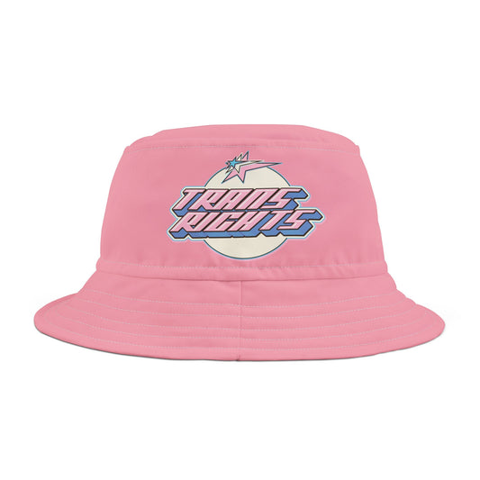 The "Trans Rights Pink Bucket Hat" by Printify is crafted from pink polyester and comes in two sizes. It features a bold, colorful "Trans Rights" graphic over a circular, pastel-colored background with a lightning bolt above the text. The hat also has visible stitching along the brim.