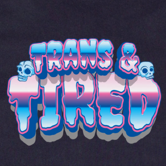 The Trans & Tired - Local hand printed t-shirt features "TRANS & TIRED" in bold, 3D letters with blue, pink, and white stripes plus two cartoon skulls on a black background inspired by the transgender pride flag.