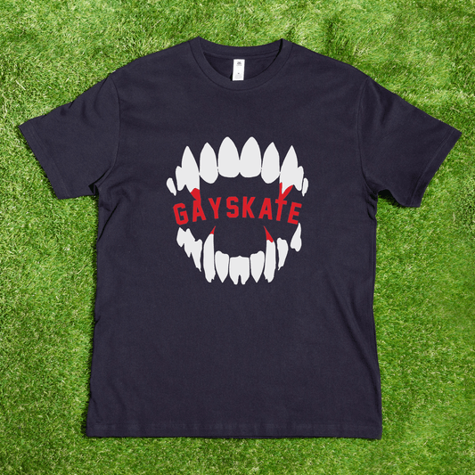 A black Vampire Skate t-shirt by a queer-owned small business lies on grass, with a white open mouth graphic and "GAYSKATE" in red across the teeth, accented by red arrows—inspired, local hand printing.