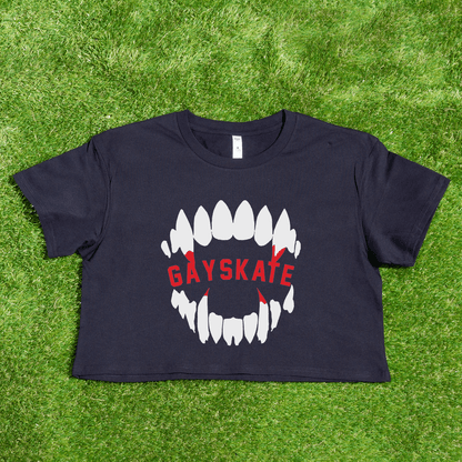 A black Vampire Skate - locally printed crop tee rests on grass, showing bold white teeth with red backdrops and "GAYSKATE" in red—perfect for fans of this queer-owned brand’s signature style.