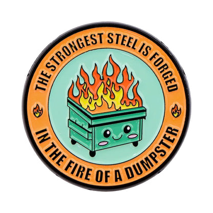 The "Very Demure Very Mindful Very Cutesy" enamel badge features a cute, smiling dumpster on fire in the center. Surrounded by bold orange text: "The strongest steel is forged in the fire of a dumpster," it's adorned with tiny flame icons for a charming look.