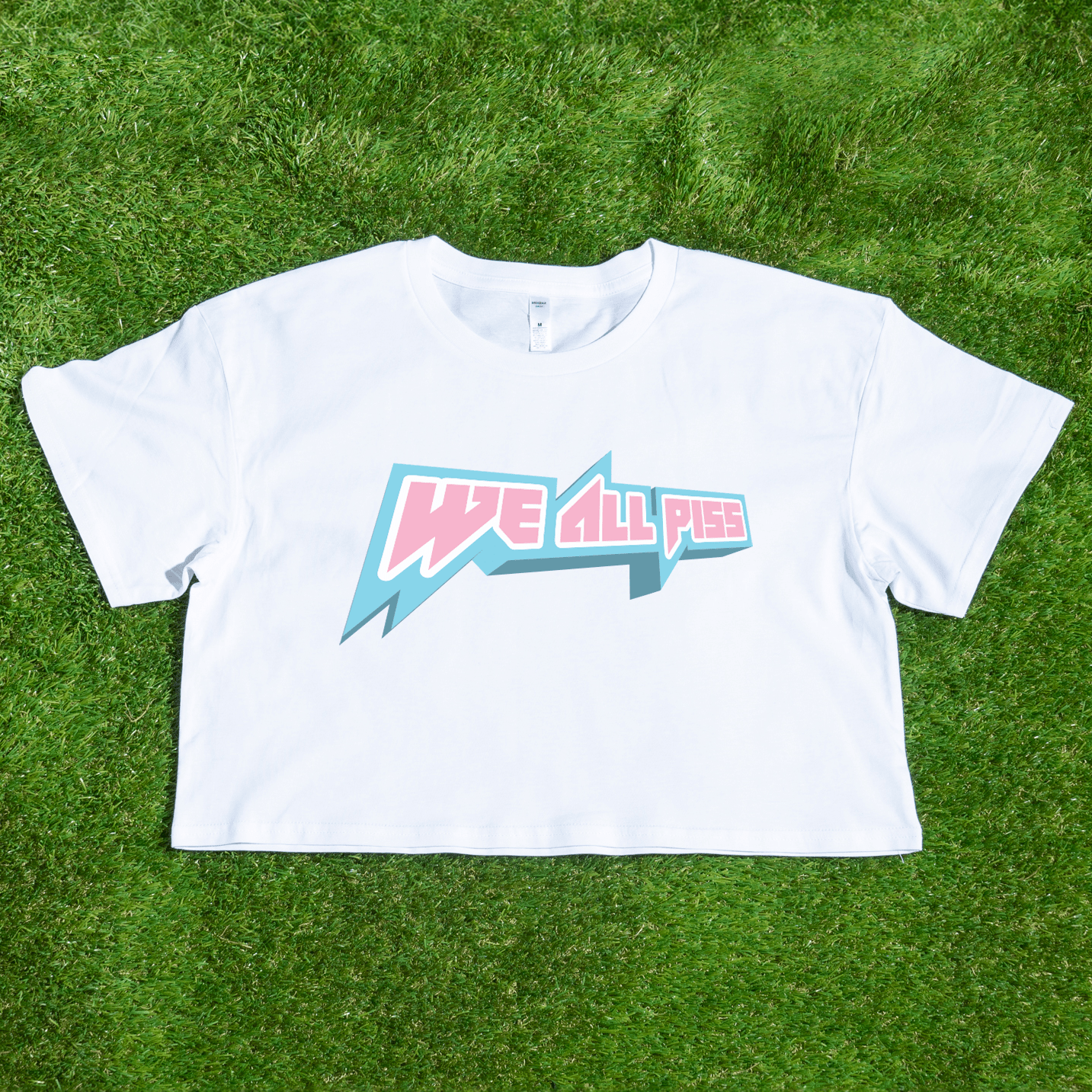 White crop t-shirt with 'We All Piss' trans rights graphic on grass