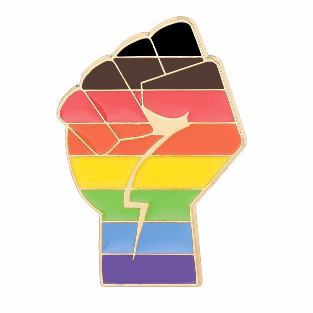 The Inclusive Rainbow Fist gold enamel pin displays rainbow stripes plus brown and black, representing LGBTQ+ pride and solidarity with marginalized groups.